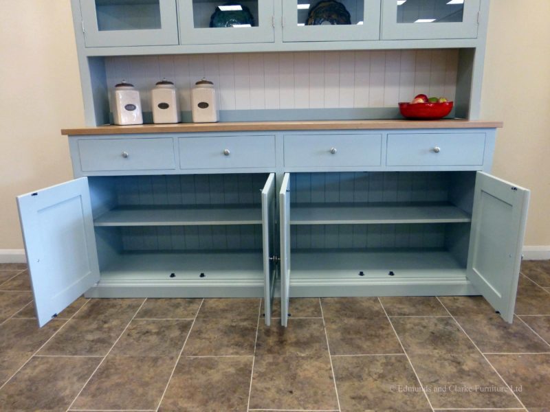 7ft Painted Half glazed dresser. Image showing cupboard doors open. Handmade with solid oak top on the sideboards, painted shelves, 4 drawers with 4 large cupboards below. 4 door glazed rack above painted in southwold sky blue and satin nickel knobs. contrasting white backboards on racking EDM021