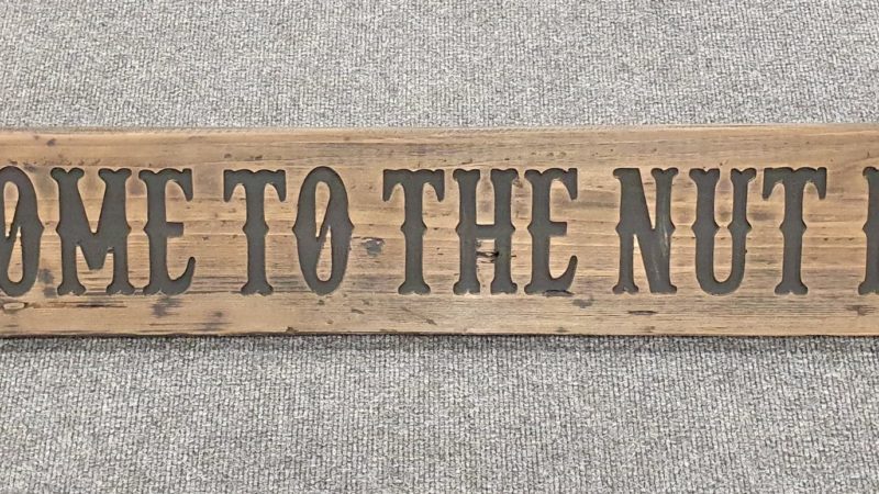 A Rustic Wooden Plaque quoting Welcome to the nut house, engraved in capital letters